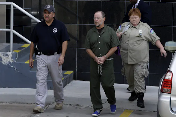 Former Enron CEO Jeffrey Skilling, with a beard and glasses, is escorted by guards from a federal courthouse on June 21, 2013, after being resentenced for his role in the energy giant's collapse.