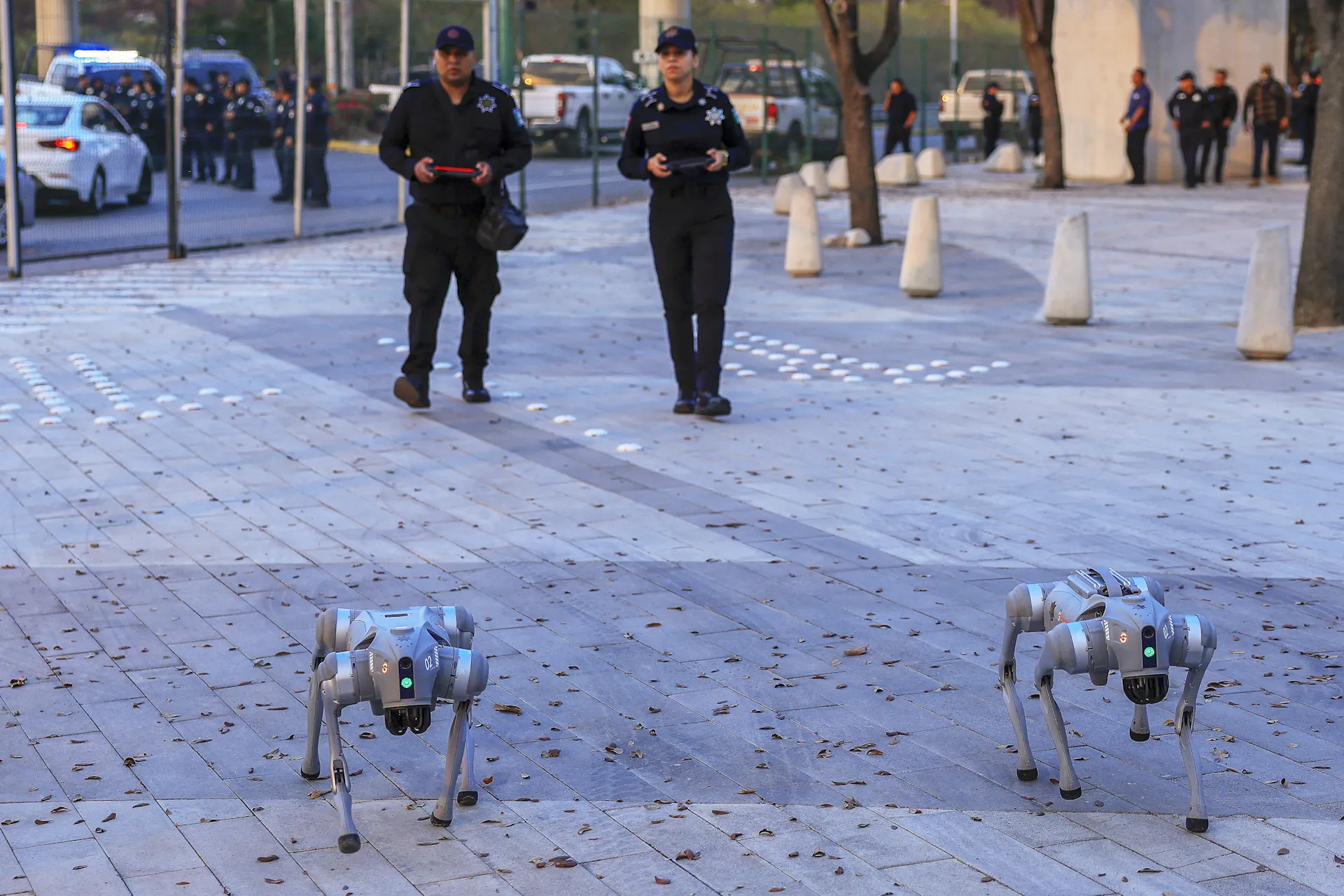 two people wearing uniforms walk behind two robotic dogs