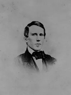 A portrait of a young man with a comb-over, pursing his lips.