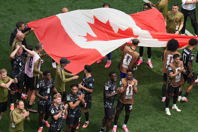 Soccer players hold up a large Canadian flag on a soccer field