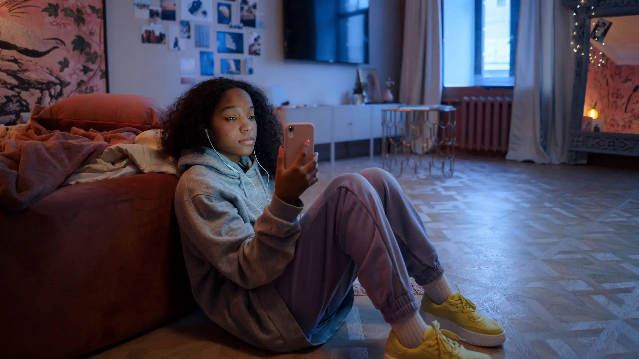 A young person sitting on the floor, looking at their phone.
