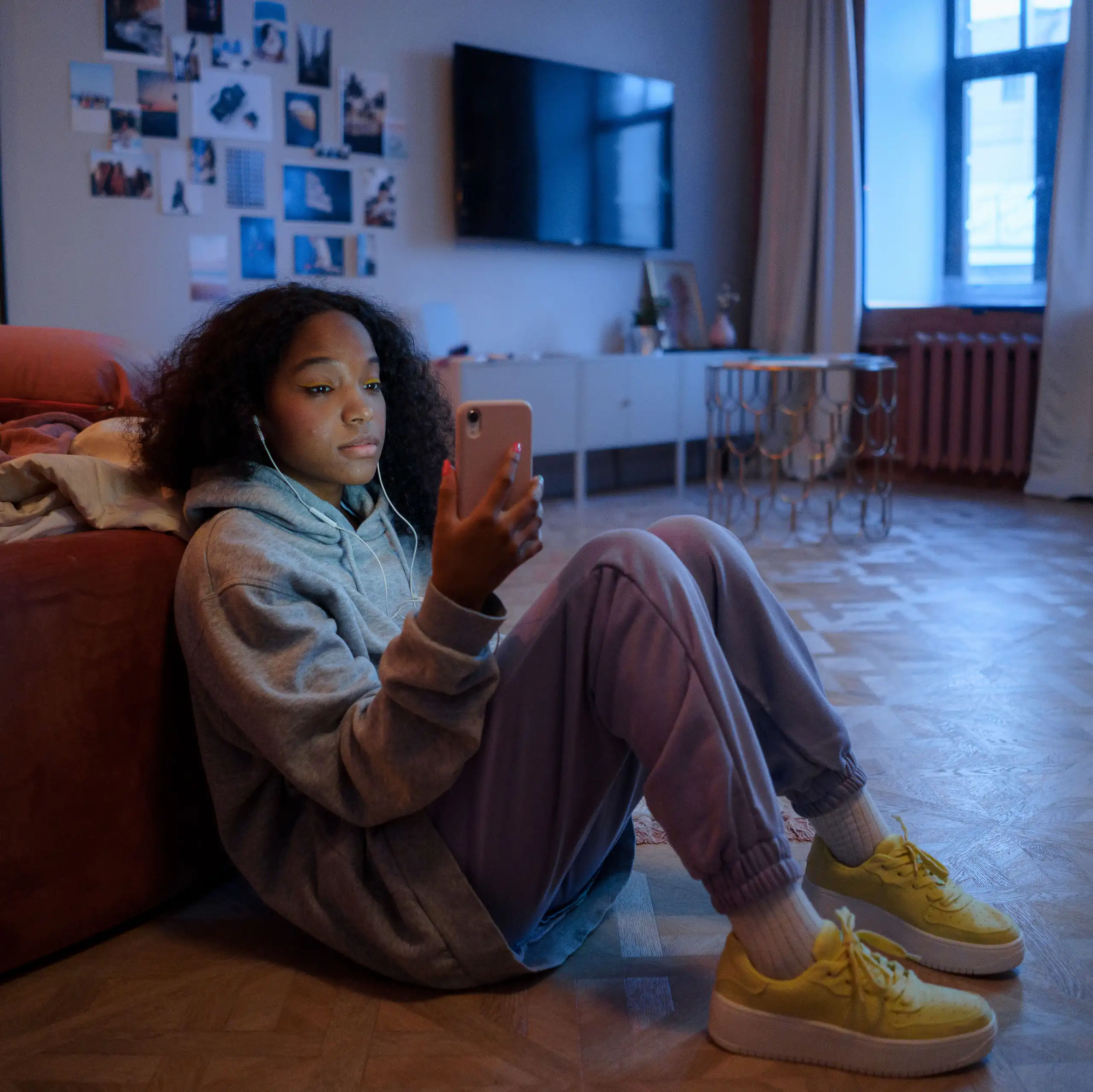 A young person sitting on the floor, looking at their phone.