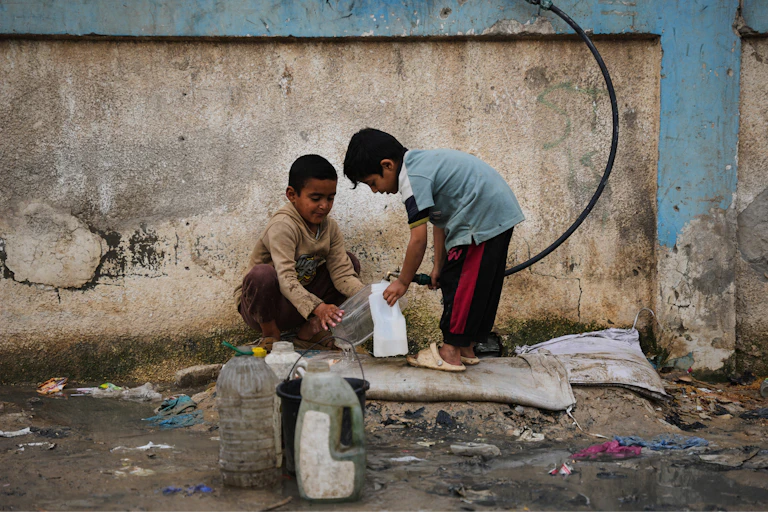 Two small boys use a hose to fill a plastic bottle up with water