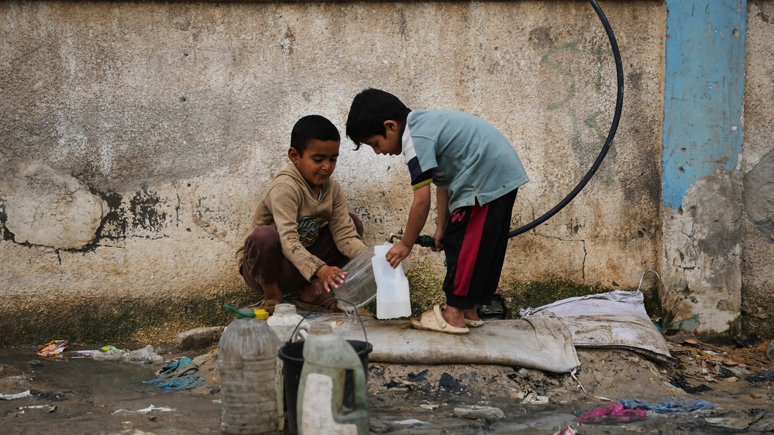 Two small boys use a hose to fill a plastic bottle up with water
