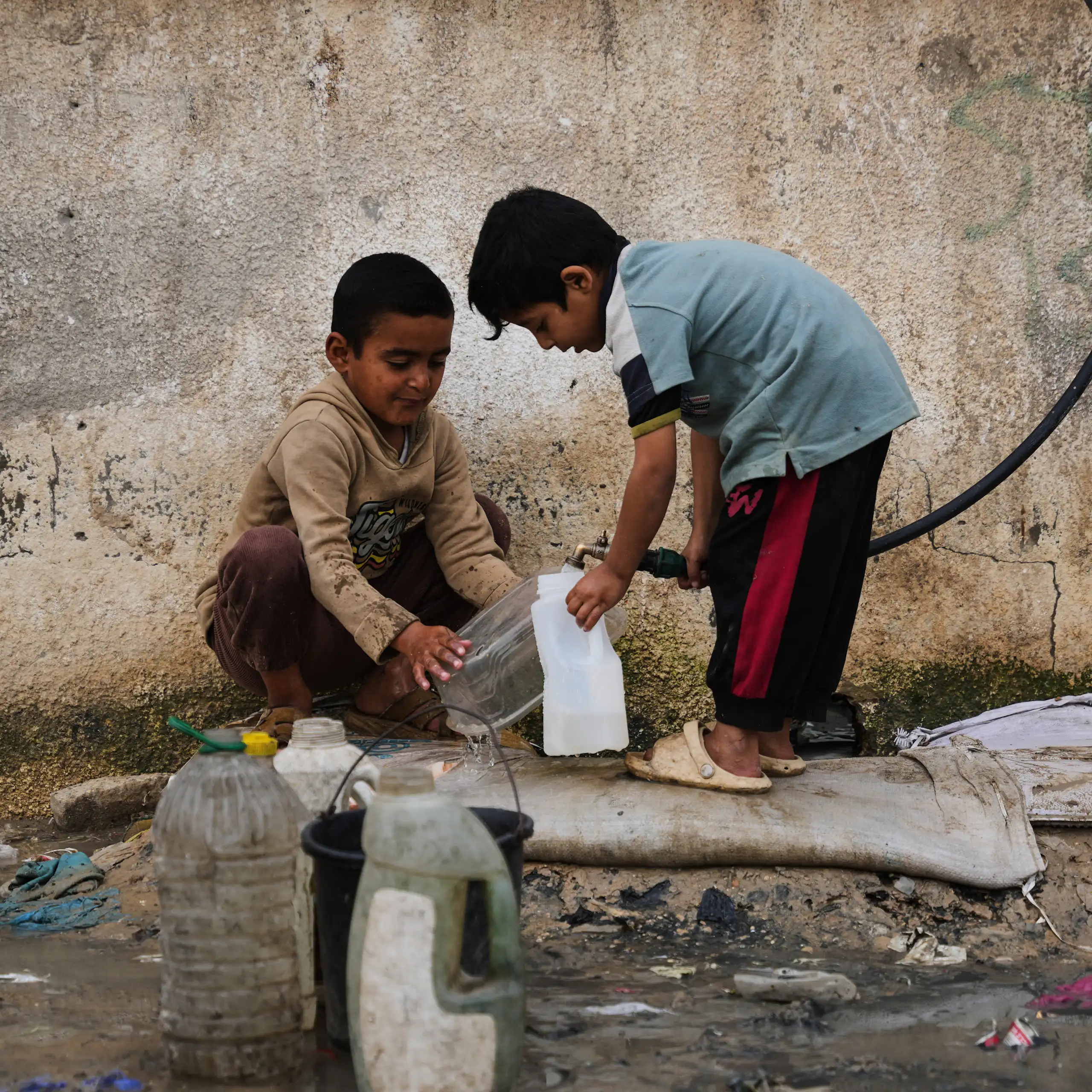 Two small boys use a hose to fill a plastic bottle up with water