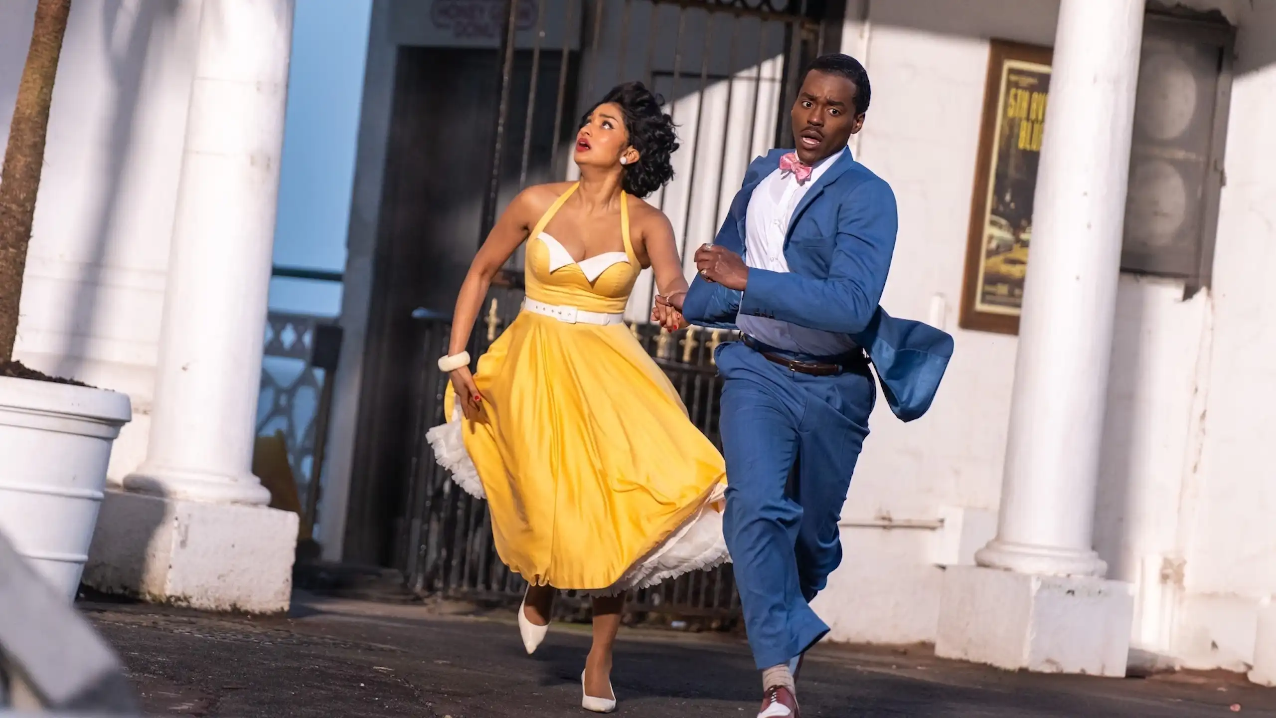 Production image: The Doctor and his assistant Belinda Chandra run away from a building.