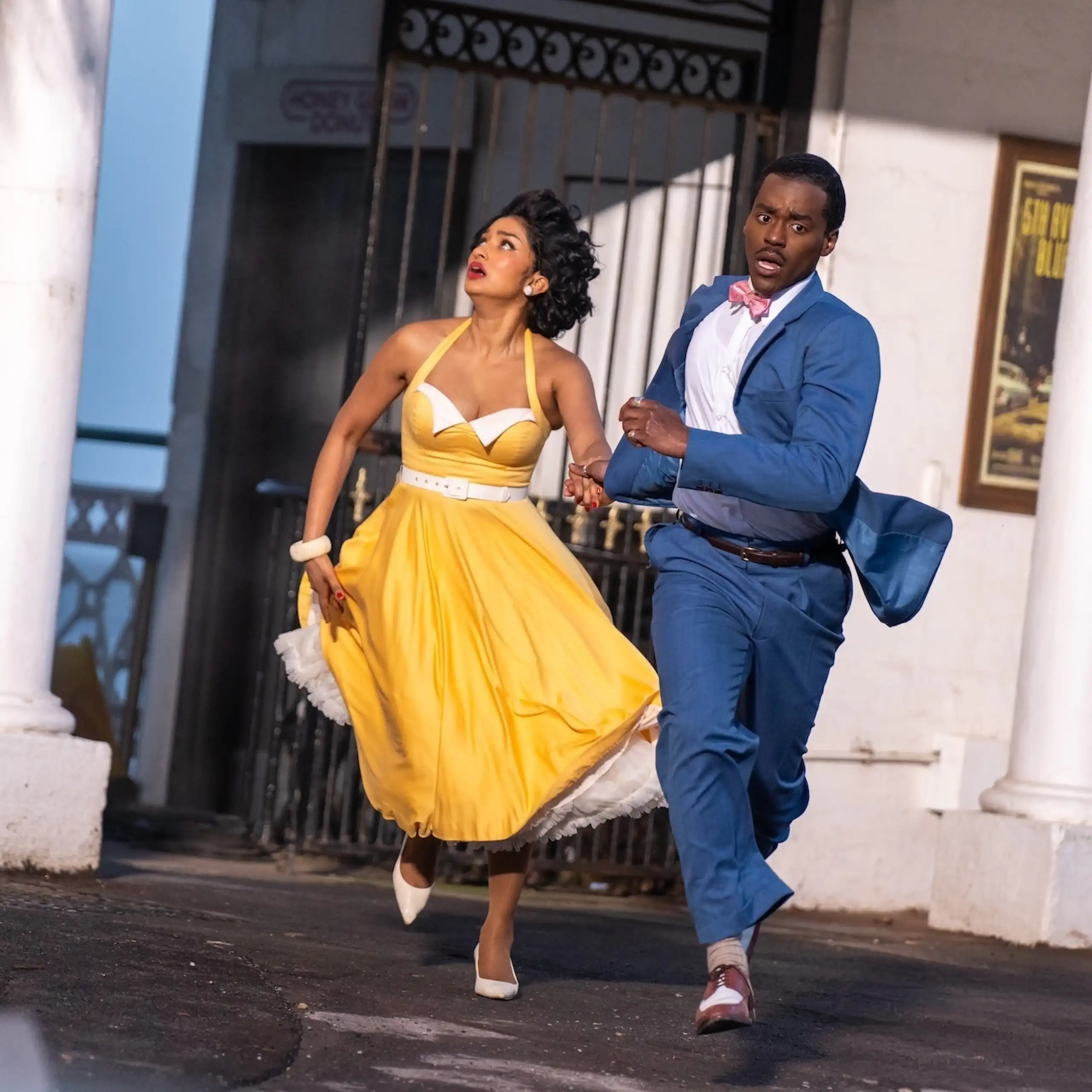 Production image: The Doctor and his assistant Belinda Chandra run away from a building.