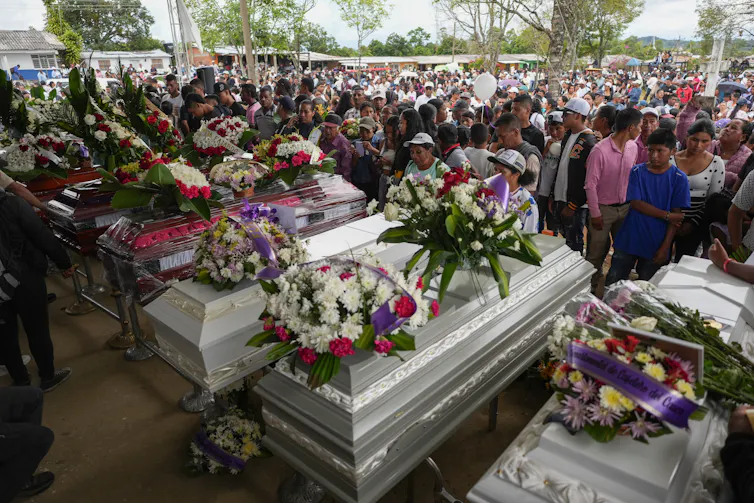 A crowd of people around coffins covered wtih flowers.