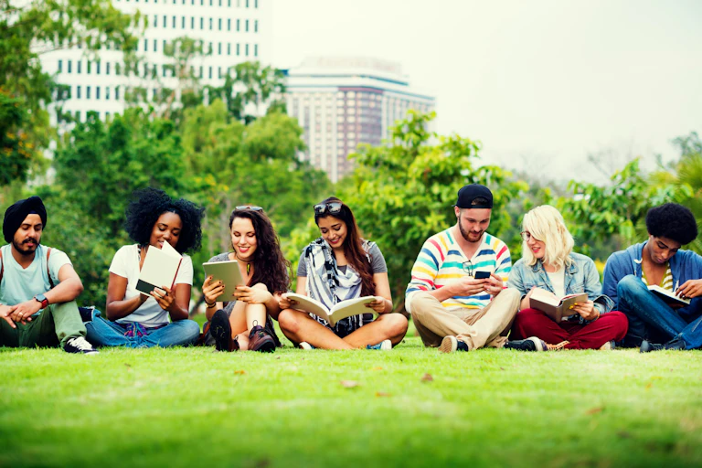 A row of university students sits in a grassy urban area.