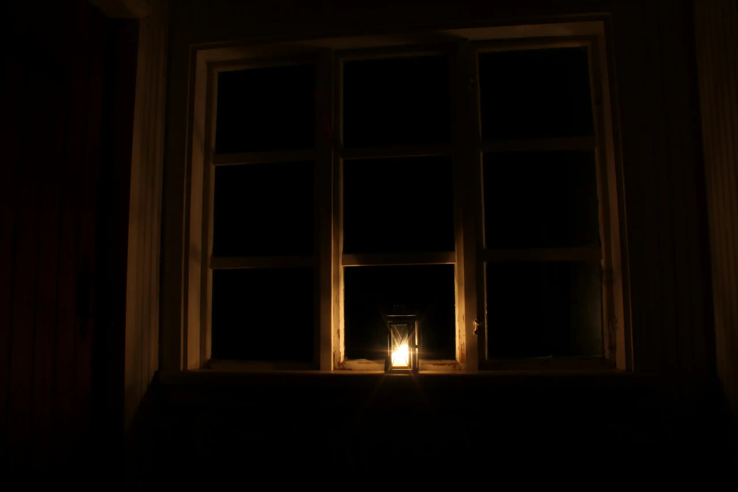 Photo d'une lanterne posée à une fenêtre dans la nuit.
