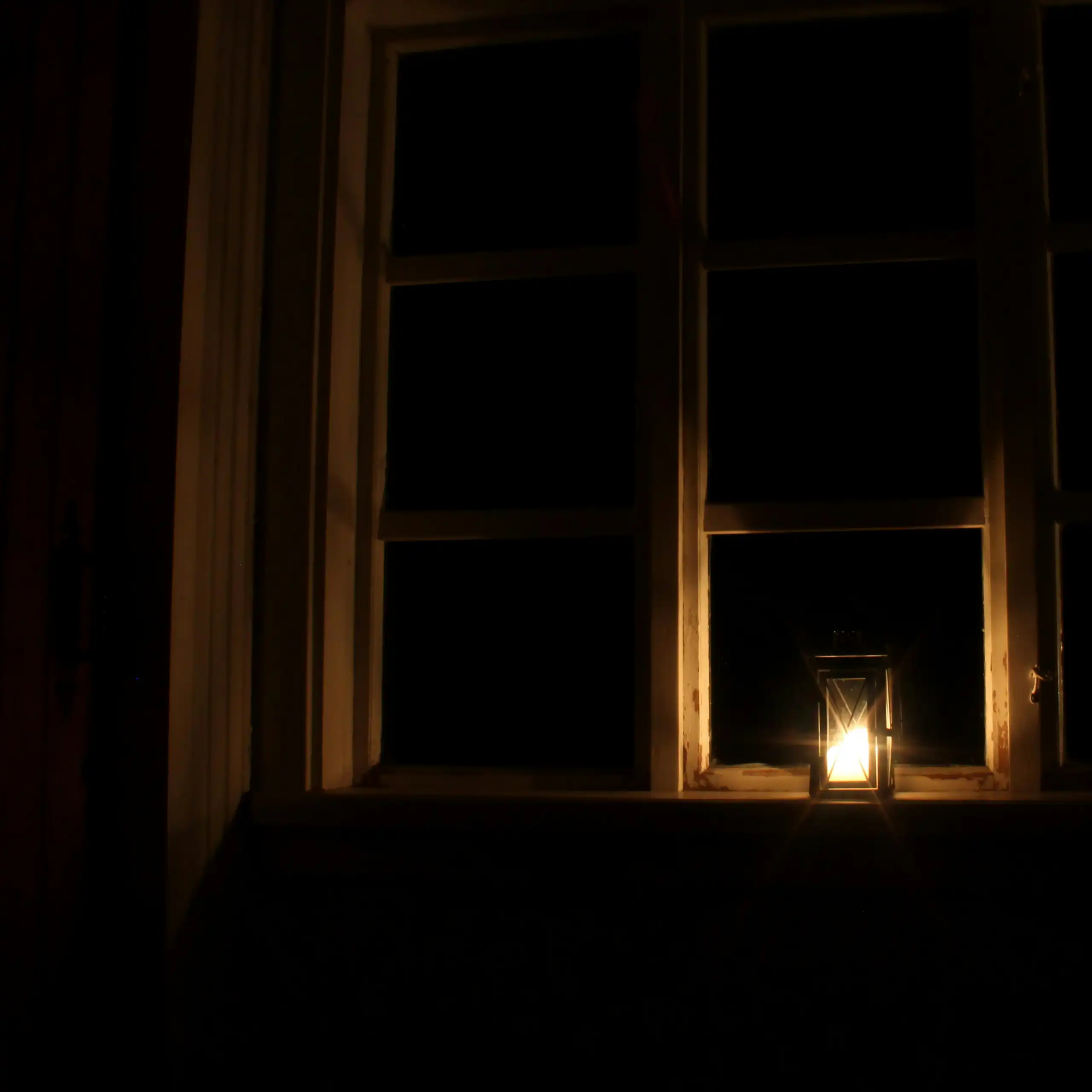 Photo d'une lanterne posée à une fenêtre dans la nuit.