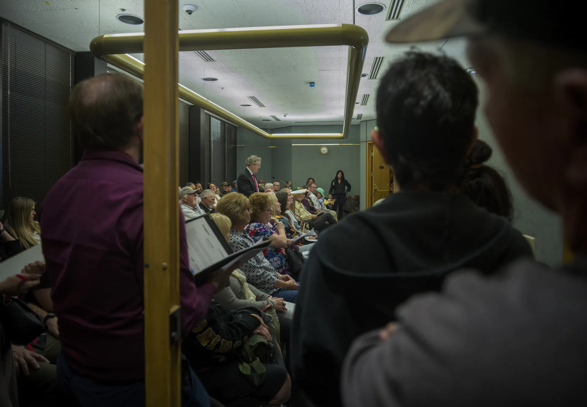 A crowd of people listen to a speaker in a public meeting room.