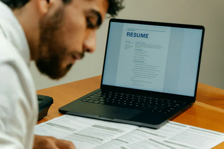 En qué se equivoca todo el mundo sobre la búsqueda de empleo moderna y qué realmente funciona 2 El documento del currículum es visible en la pantalla del portátil. Delante, un hombre consulta documentos sobre una mesa con un portátil encima.
