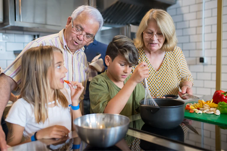Grandparents teaching grandchildren to cook in a modern kitchen, sharing family time and culinary skills.