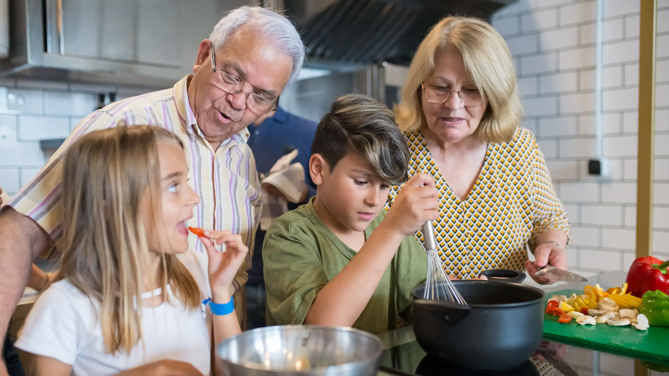 Grandparents teaching grandchildren to cook in a modern kitchen, sharing family time and culinary skills.