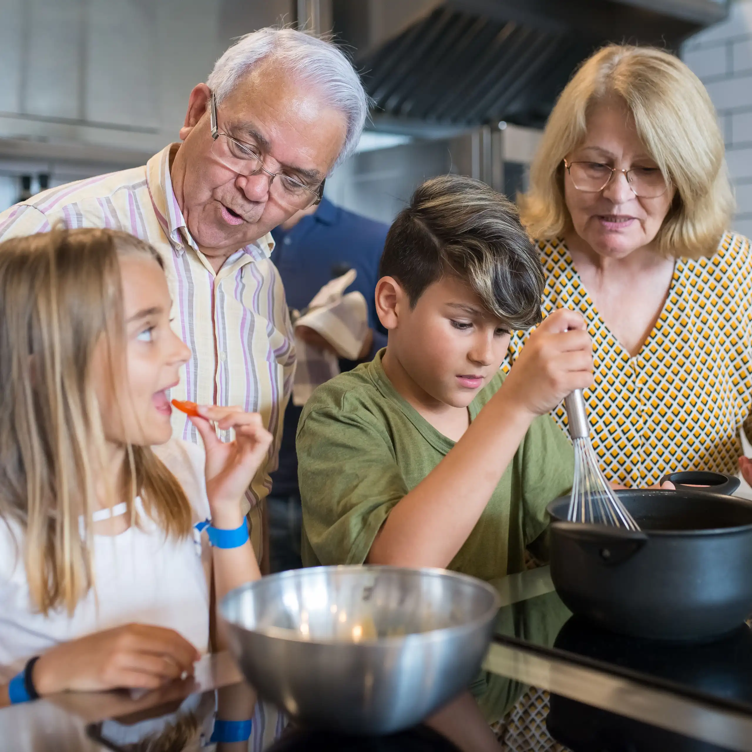 Grandparents teaching grandchildren to cook in a modern kitchen, sharing family time and culinary skills.