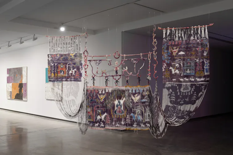 Three weavings hang in a gallery.