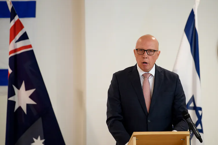 a bald man in a suit between Australian and Israeli flags