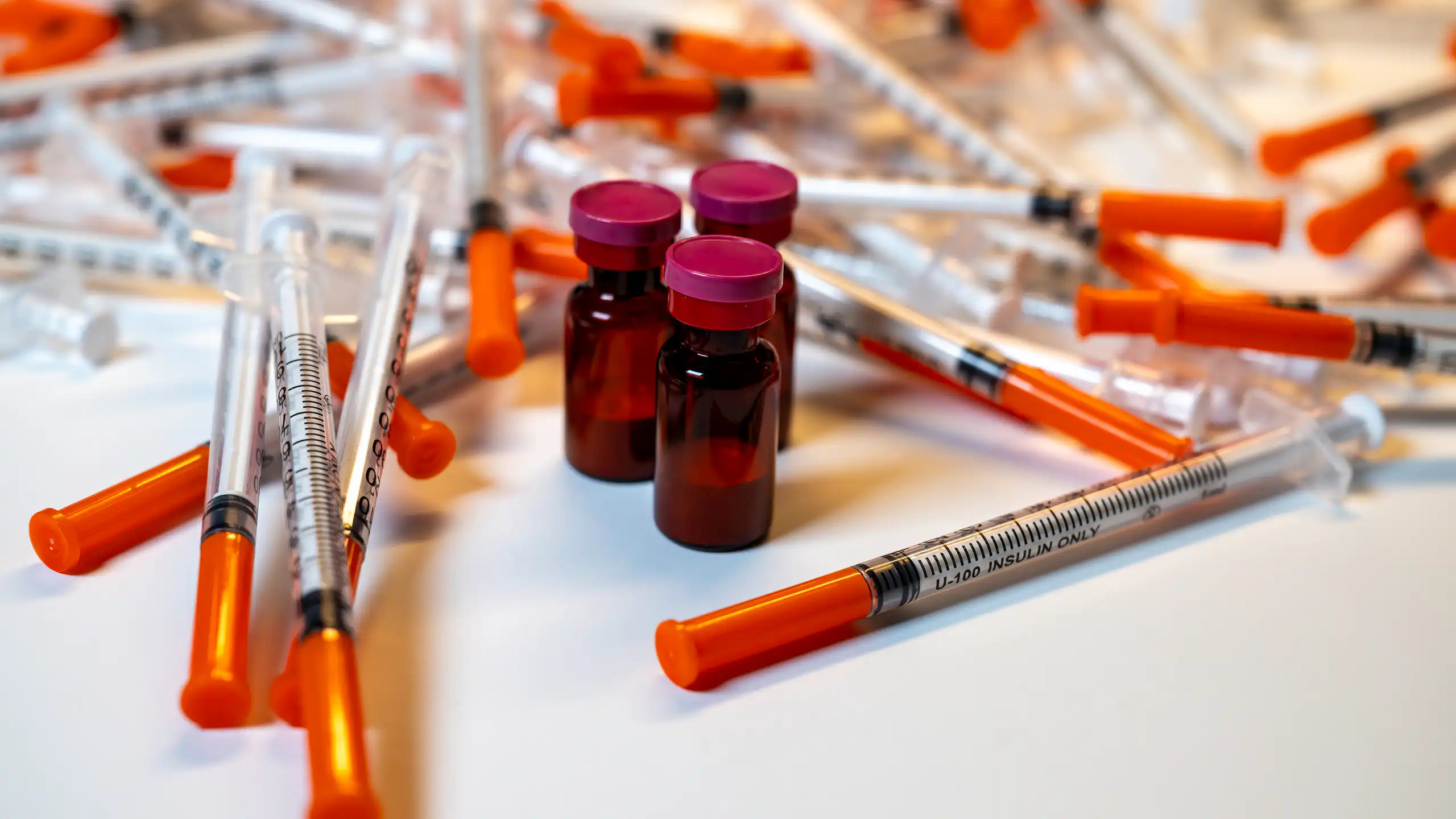 Phials of peptide drugs surrounded by syringes.