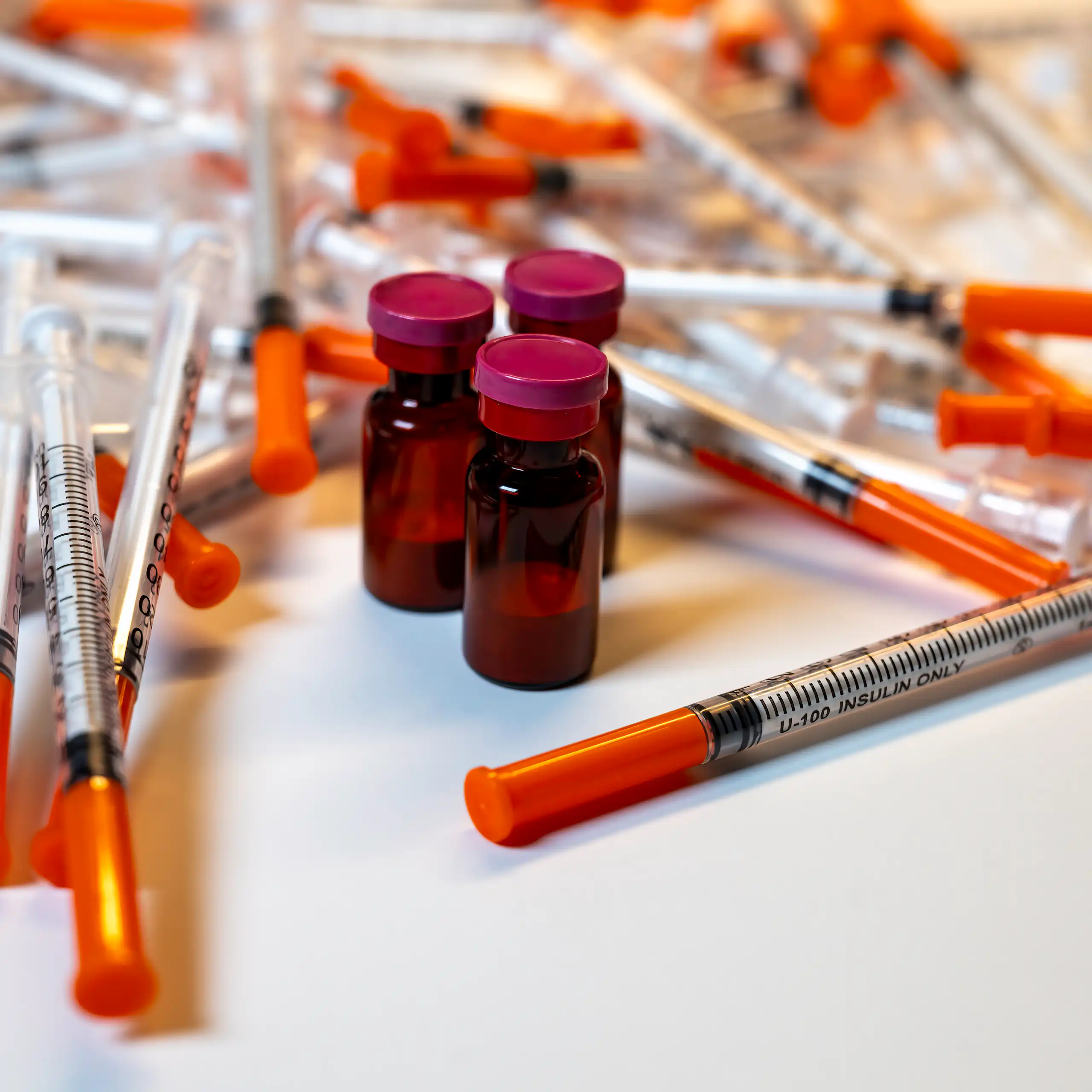 Phials of peptide drugs surrounded by syringes.