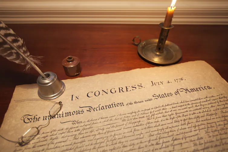 Stock photograph with a replica of the Declaration of Independence with a quill and a candle.