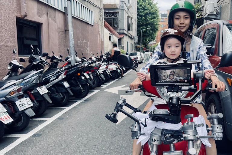 A young girl and her mother on a motorbike in Taiwan, being filmed by an iphoe