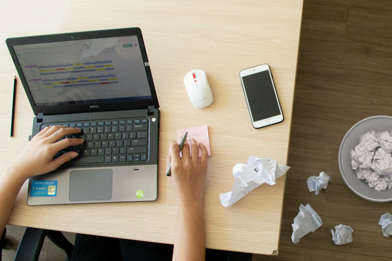 A person at a laptop seen with many crumpled papers.