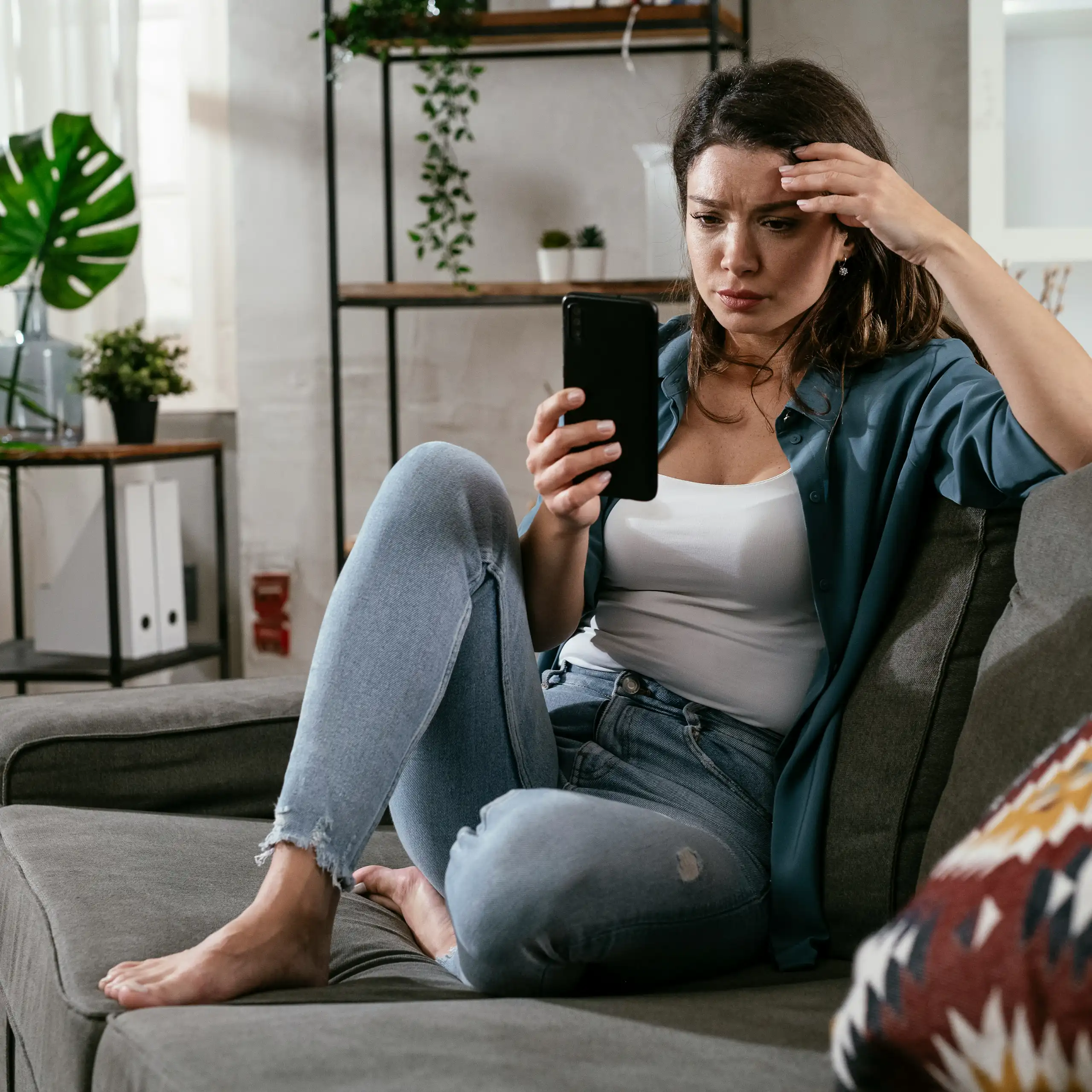 A woman sitting on a sofa looking at a phone screen with a puzzled expression