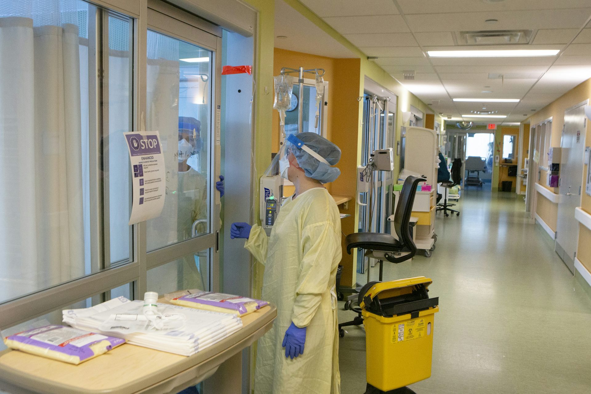 Una persona con EPI amarillo y azul en el pasillo de un hospital