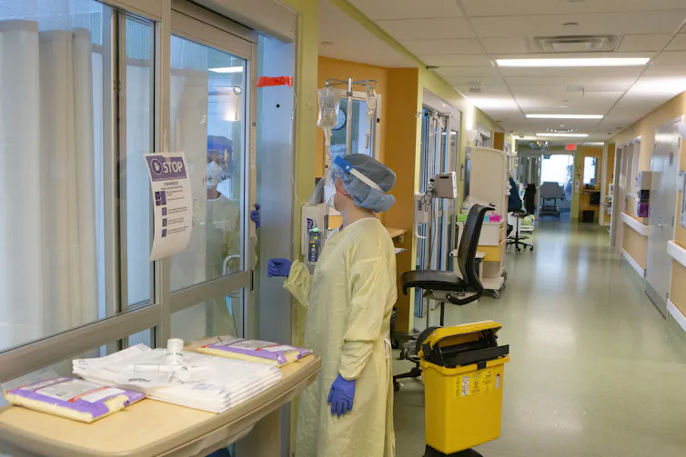 Una persona con EPI amarillo y azul en el pasillo de un hospital
