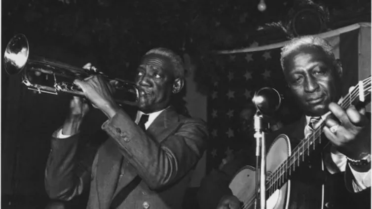 black-and-white photo of a trumpet player and guitar player on stage in front of an American flag
