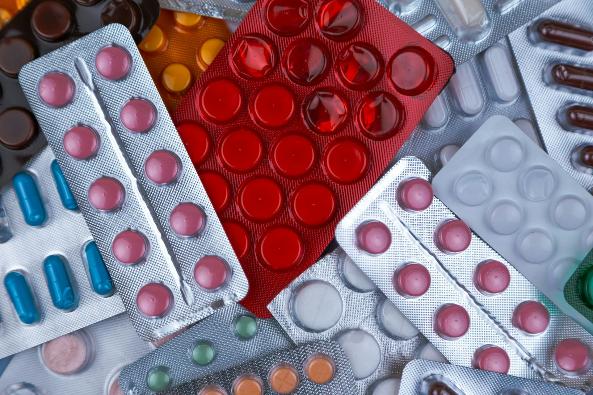 A pile of prescription pill packs, containing white, red, pink, orange and green drugs.