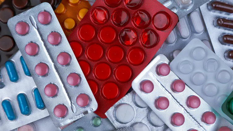 A pile of prescription pill packs, containing white, red, pink, orange and green drugs.