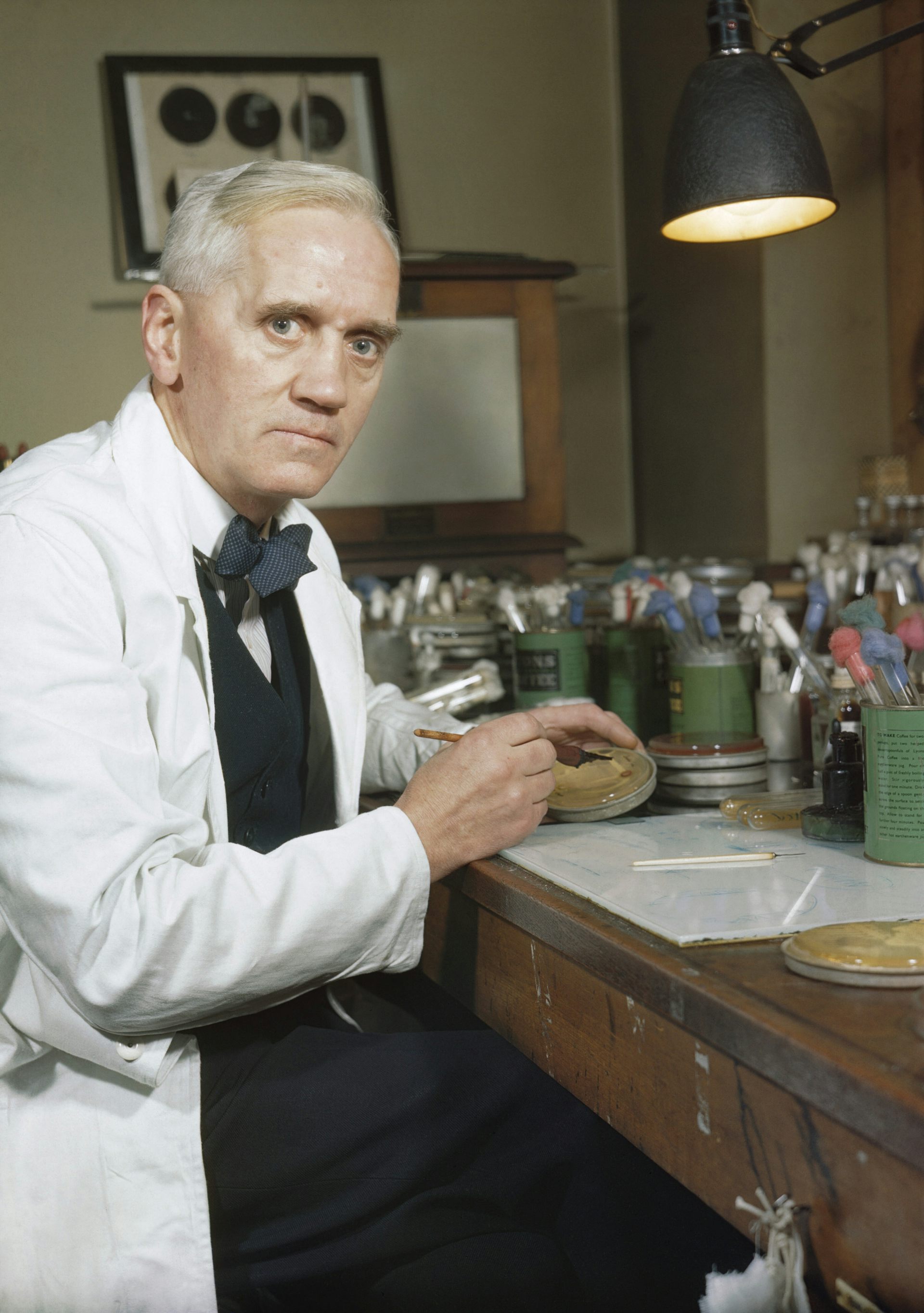 A man in a white coat with a serious face at a desk
