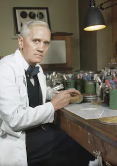 A man in a white coat with a serious face at a desk