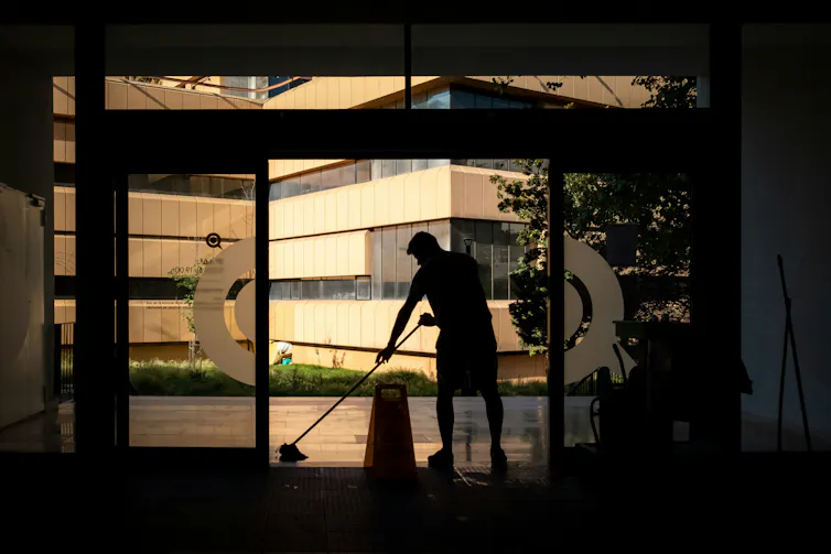 A silhouette of a male cleaner, standing in front of a large glass window