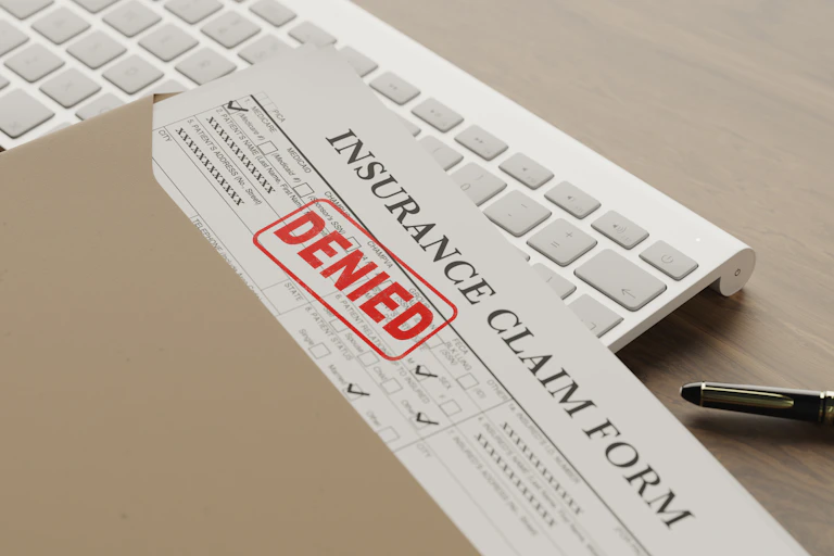 An envelope from which an Insurance claim document peeks out, stamped DENIED.