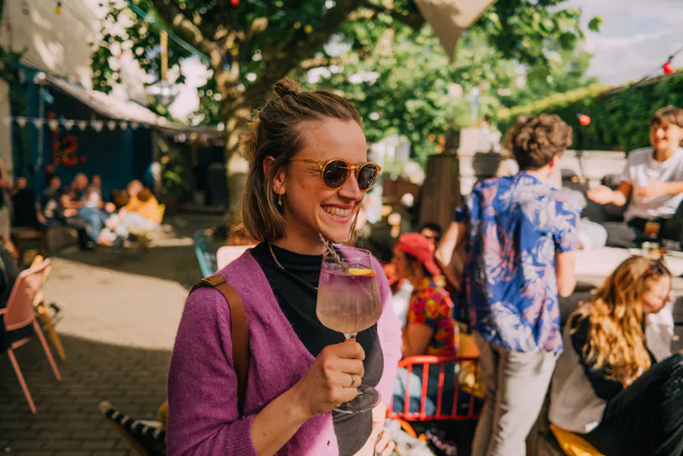 Smiling young woman holding an alcoholic drink at a festive outdoor event.