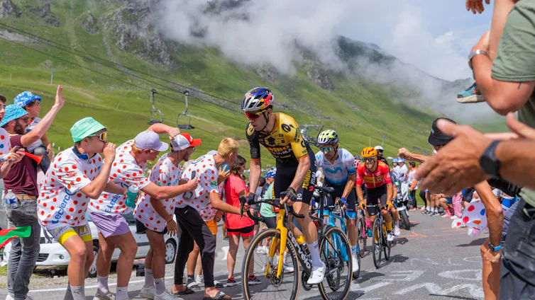 Unos ciclistas en una competición con montañas de fondo y aficionados a ambos lados de la carretera.