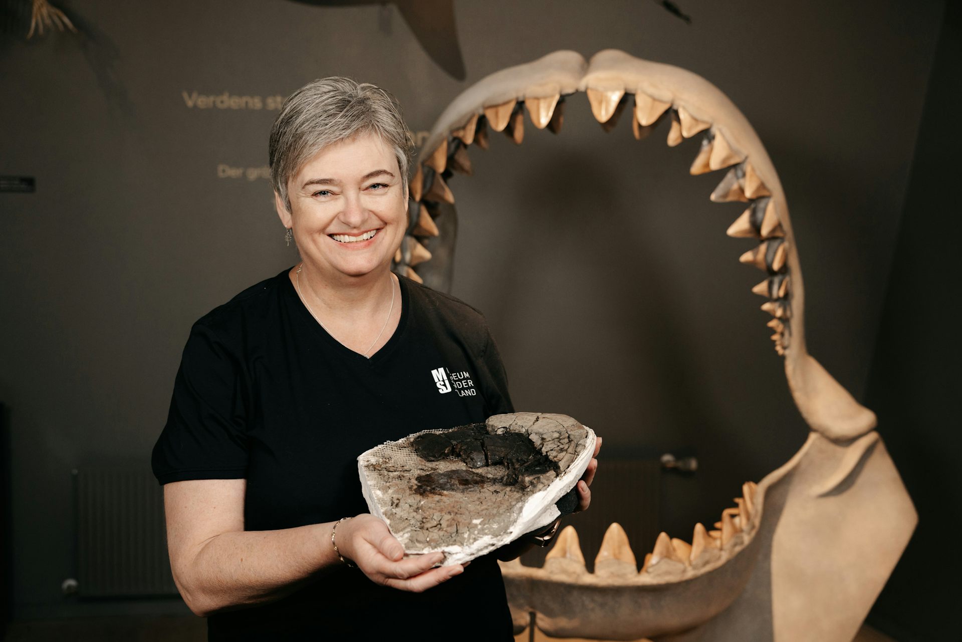 Woman holding giant piece of bone with reconstructed shark jaws in the background.