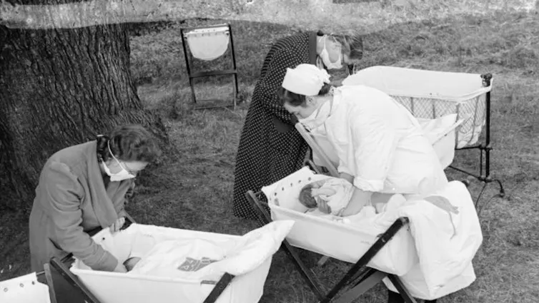 A black and white archival photograph of women tending babies in a garden.