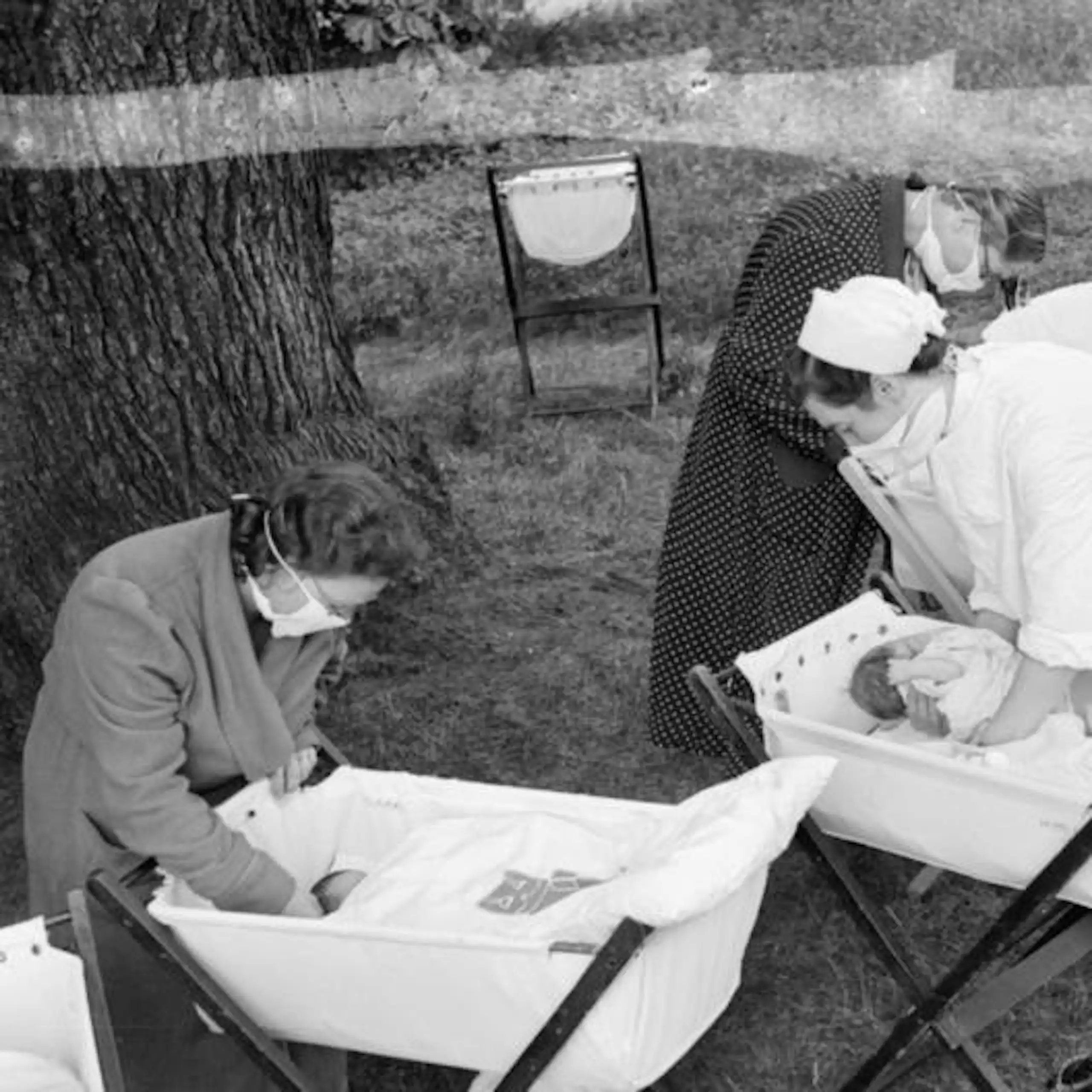 A black and white archival photograph of women tending babies in a garden.