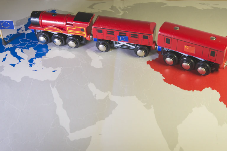 Morceau de planisphère visualisant, à l’ouest, les pays membres de l'Union européenne, signalés en bleu, et, à l'est, la Chine, en rouge. Un train rouge portant les deux drapeaux (UE et Chine) circule de l'est à l'ouest