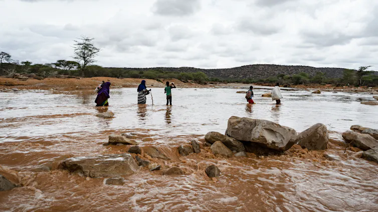 Una familia cruza un río peligroso durante unas fuertes inundaciones, con un cielo espectacular