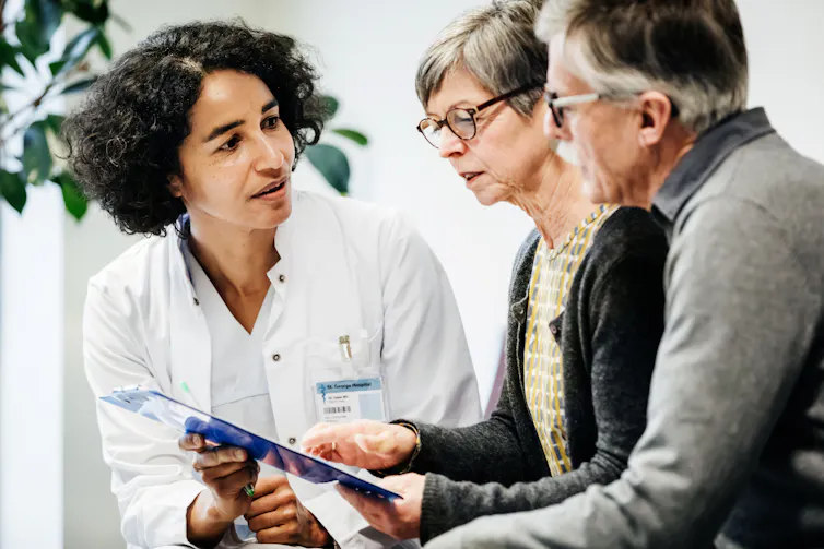 A doctor shows an older couple some test results on a tablet.
