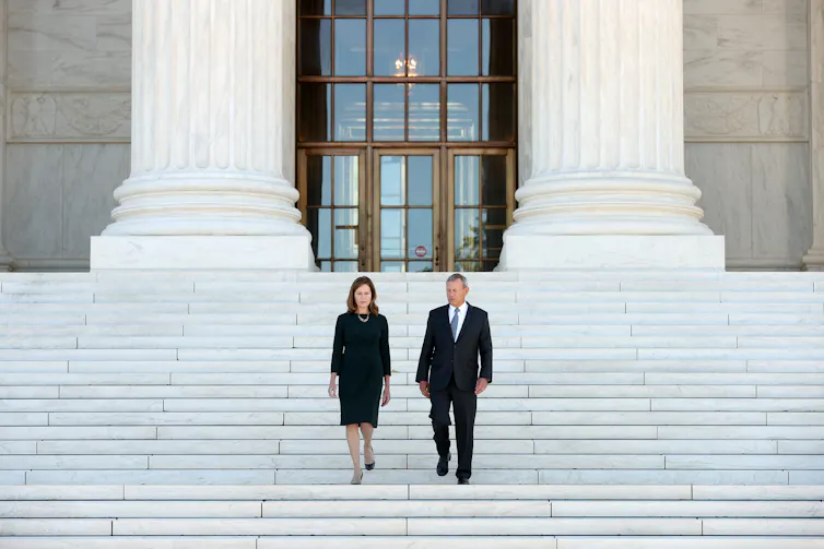 A man and a woman, both in black clothes, walking down a huge set of steps in front of a large building with pillars.