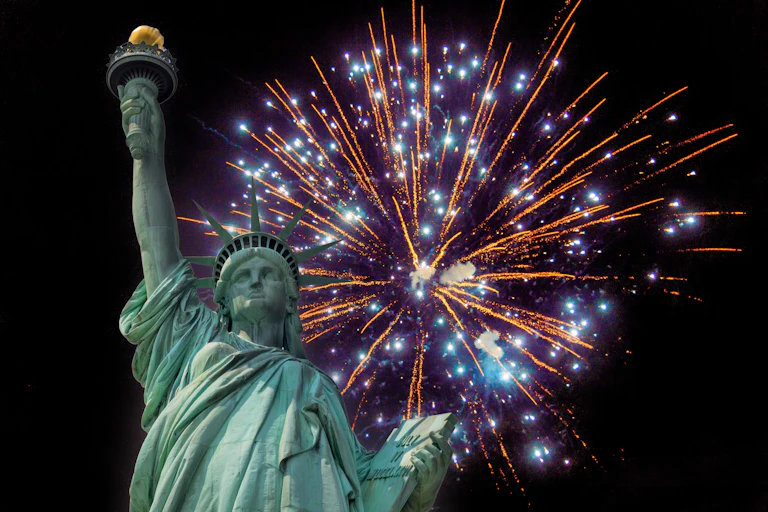 The Statue of Liberty against a skyline of 4th of July fireworks in New York.