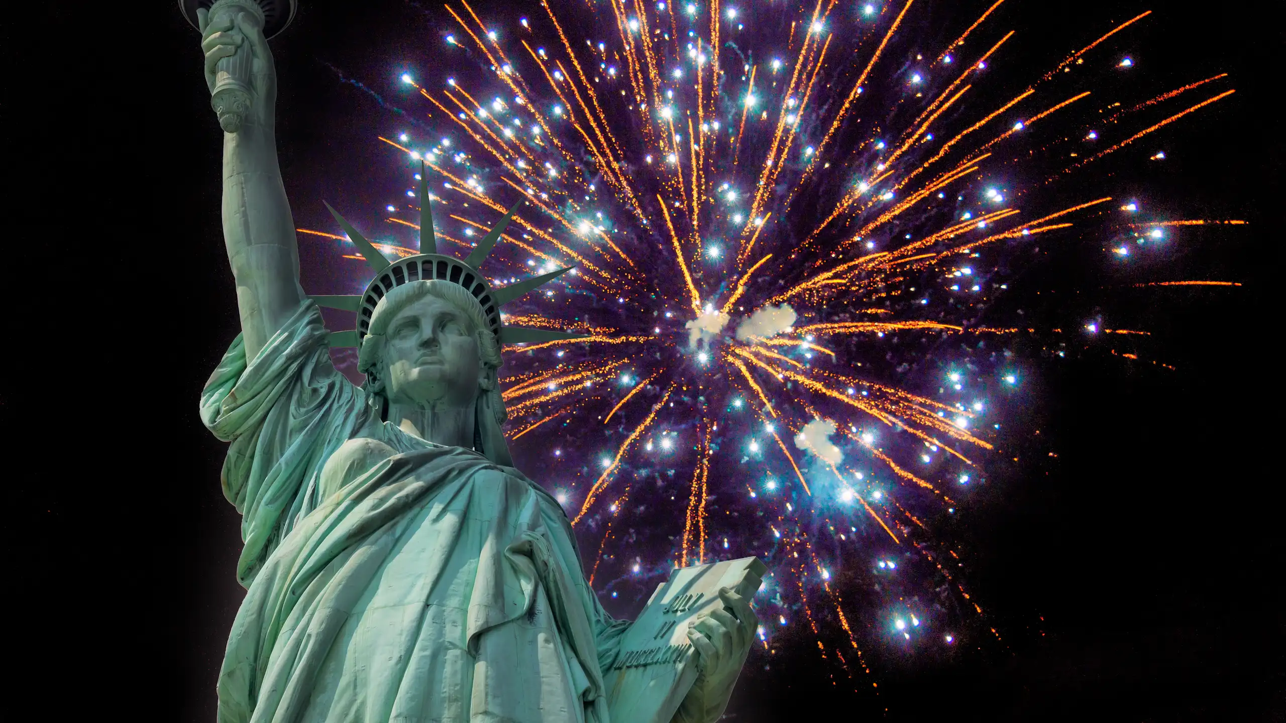 The Statue of Liberty against a skyline of 4th of July fireworks in New York.