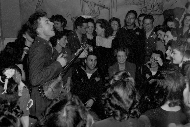 black and whgite photograph of a man singing and playing banjo in a crowded room