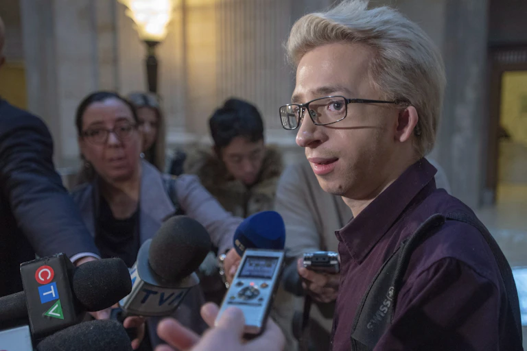 A man with blonde hair and glasses speaks to the media.